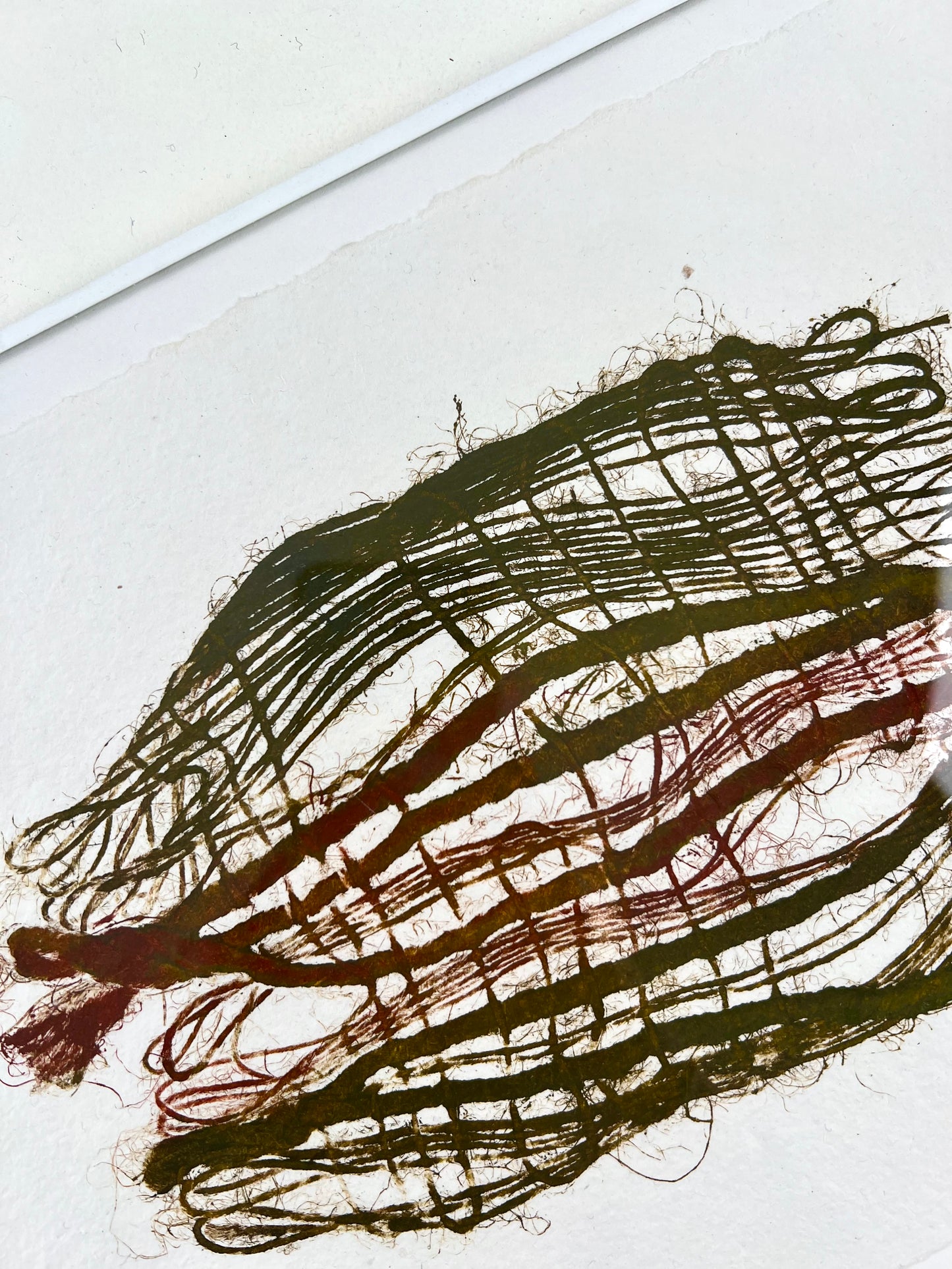 Détail d'une estampe de tissage verte et bordeaux encadrée sur papier artisanal