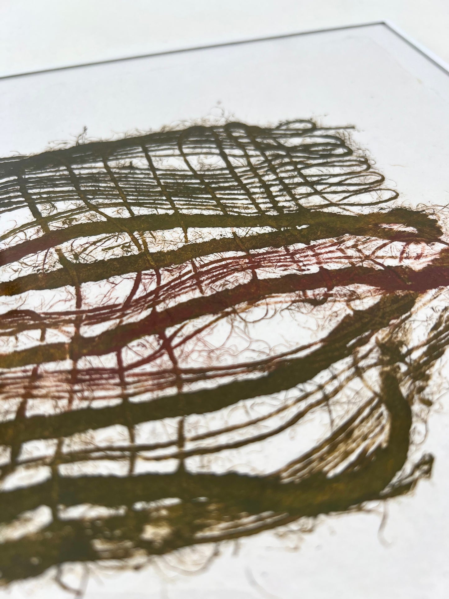 Détail d'une estampe de tissage verte et bordeaux encadrée sur papier artisanal
